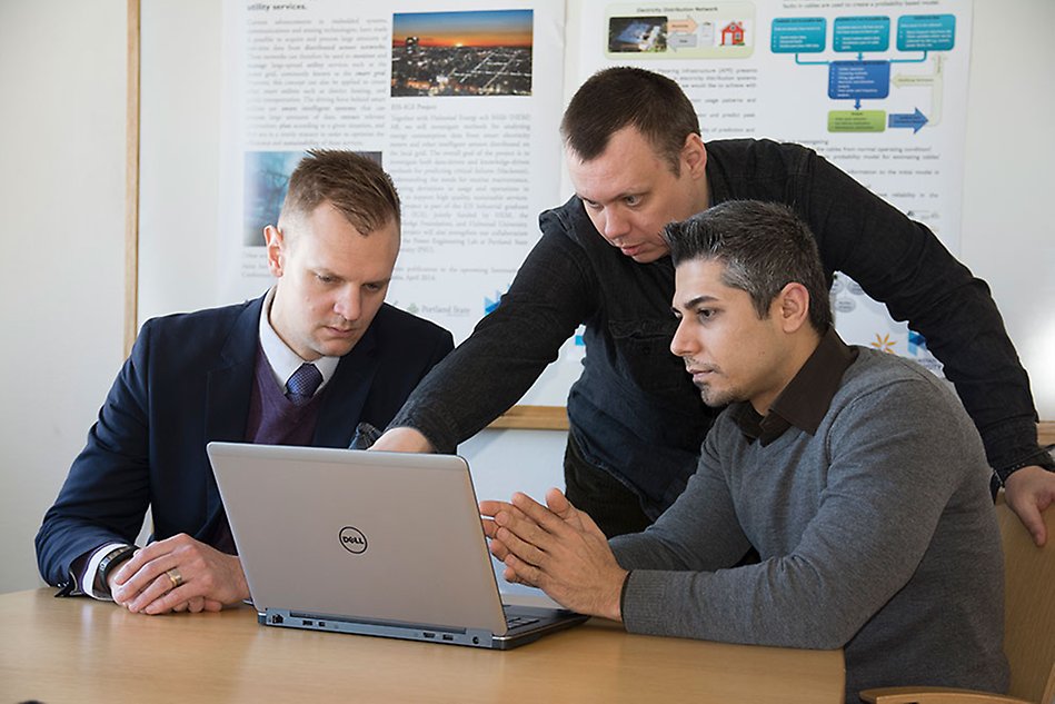 Three men discussing in front of a computer screen.
