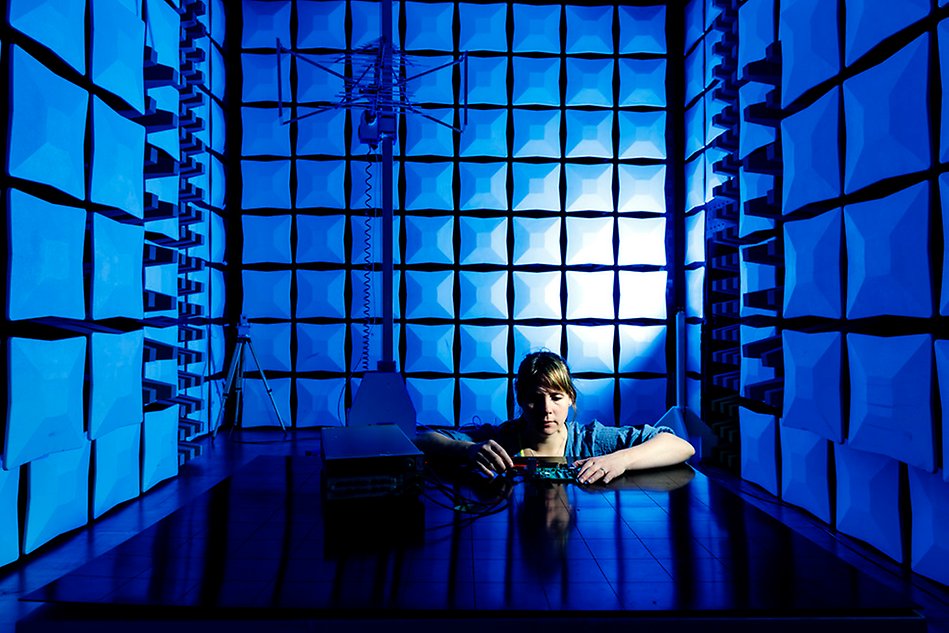 Woman sitting at table in an electronic test lab and holding an object. Blue light in the room. Photo.