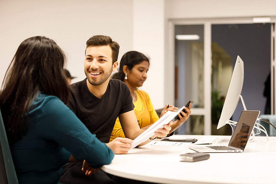 A man and a woman are laughing and talking to each other, another woman is sitting at a computer in the background. Photo. 