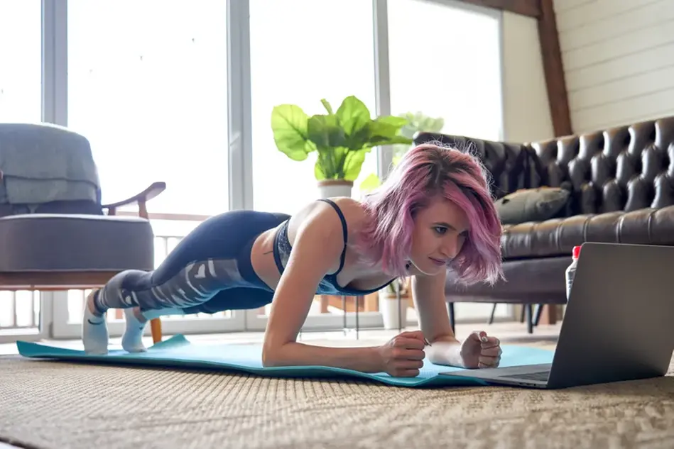 En kvinna står i så kallad planka på en yogamatta. Foto