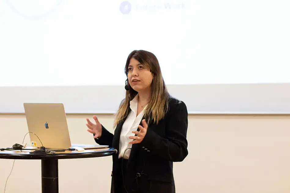 A woman stands infront of a podium, gesticulates with her hands and talks.
