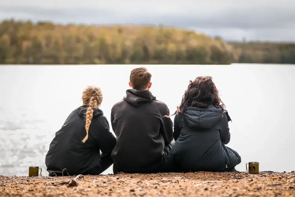Tre personer sitter med ruggarna mot kameran framför en stor sjö. 