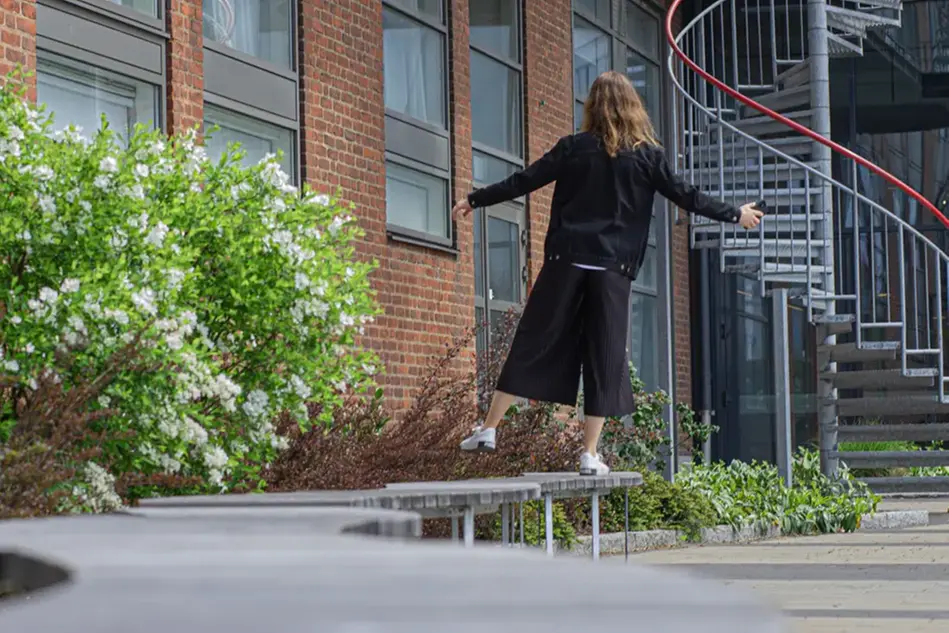 En kvinna balanserar på ett ben på en parkbänk. Foto