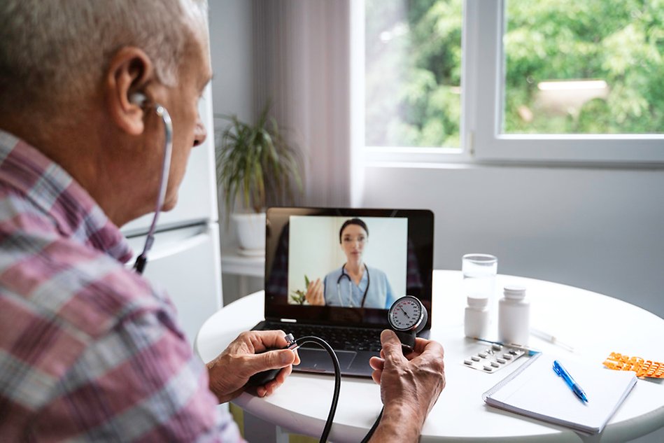 A man checks his vitals while speaking to a doctor on a screen.