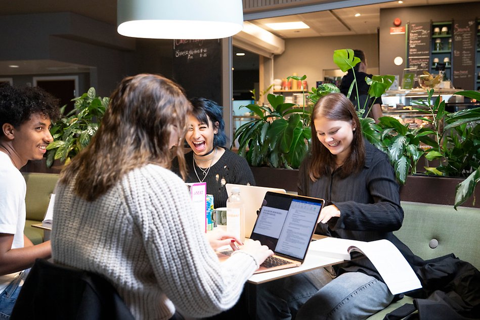 Four young people sitting by a table, laughing. Photo. 