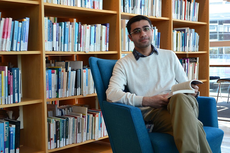 Man sitting in a library, holding a book and looking into the camera