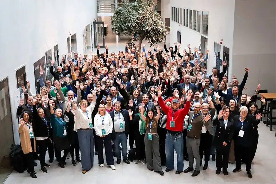 A large group of people standing in an open space at campus, cheering. Photo.