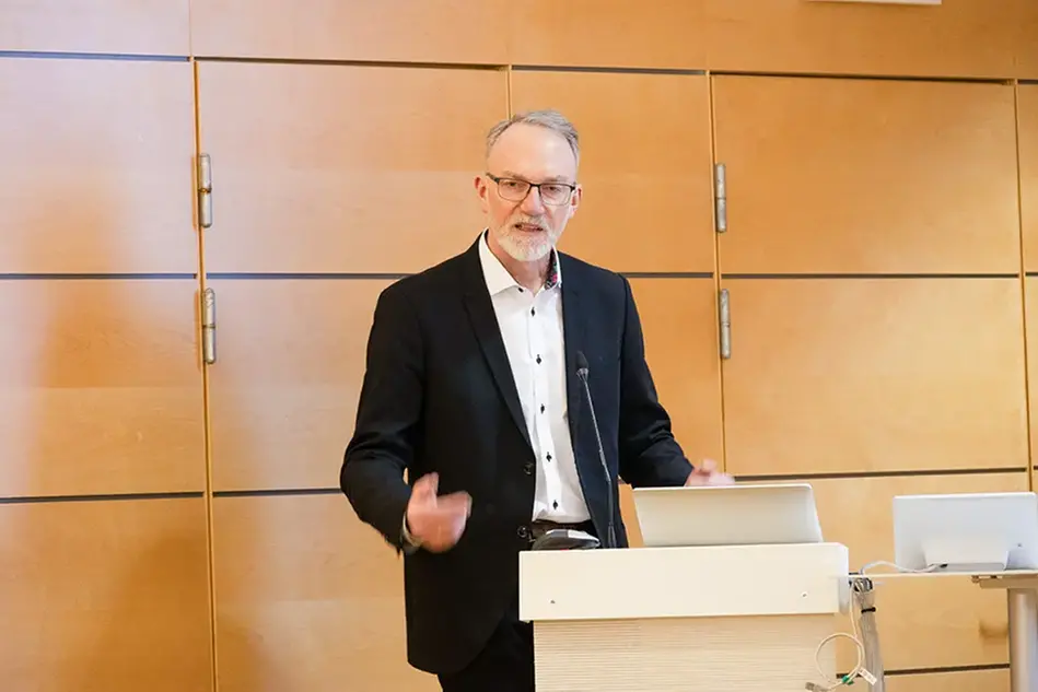 Person står vid ett podium och ser ut att tala till en publik. 