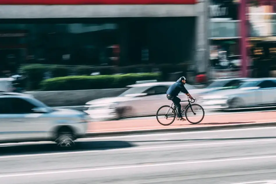 A man on a bicycle cycles on a big road between cars.