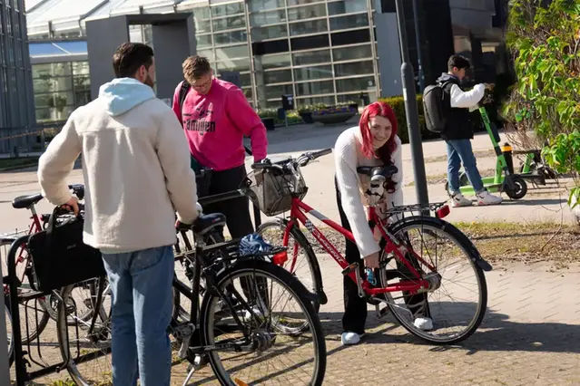 Tre personer står vid varsin cykel i utomhusmiljö. Foto