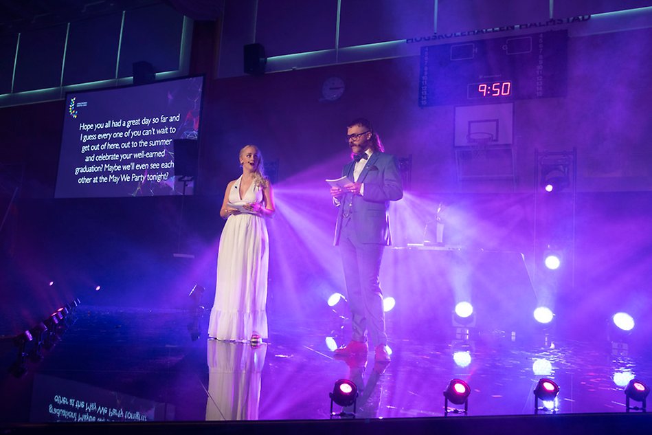 A women in a dress and a man in a suite are standing on a stage with bright background lights.Photo.