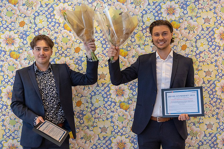 Two students hold flowers and diplomas and looks into the camera.