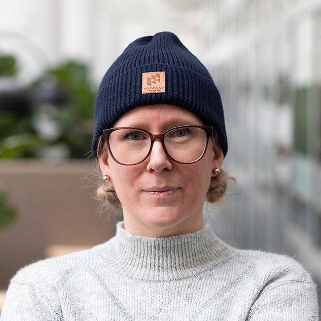 A person with glasses looks into the camera and has a blue hat on her head. Photo.