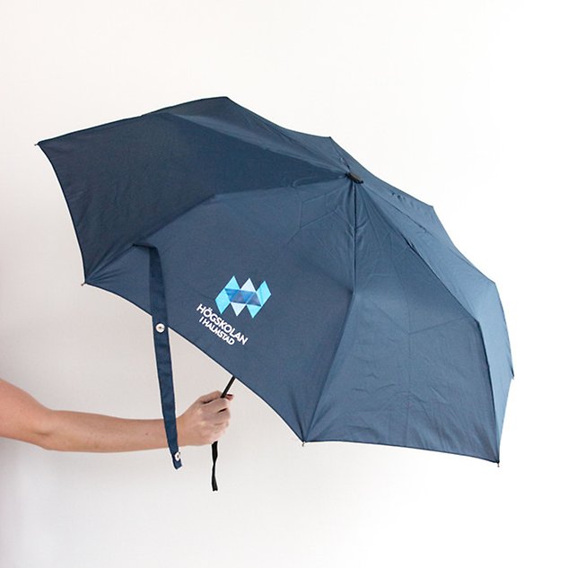 En hand som håller upp ett mörkblått, utfällt paraply. Foto.