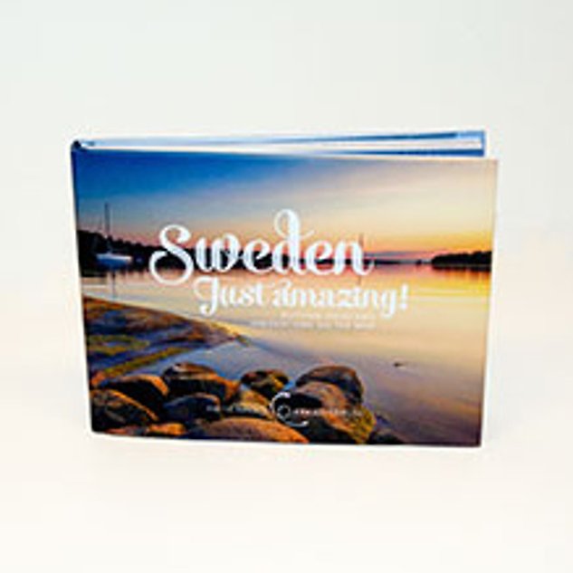 En bok med en bild på vatten och solnedgång på omslaget och texten ”Sweden just amazing”. Foto. 