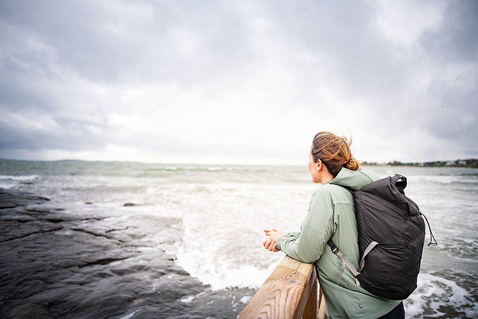 A person stands looking out over the sea. It is windy, and there are waves. 
