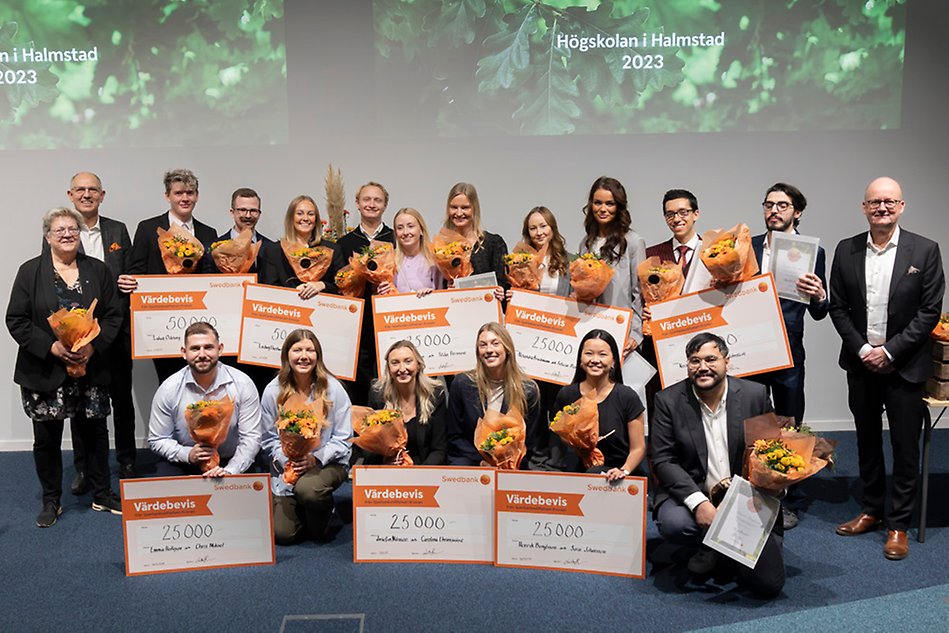 Studenter, jury och rektor poserar och ler mot kameran. Studenterna håller upp stora checkar och en varsin bukett blommor.