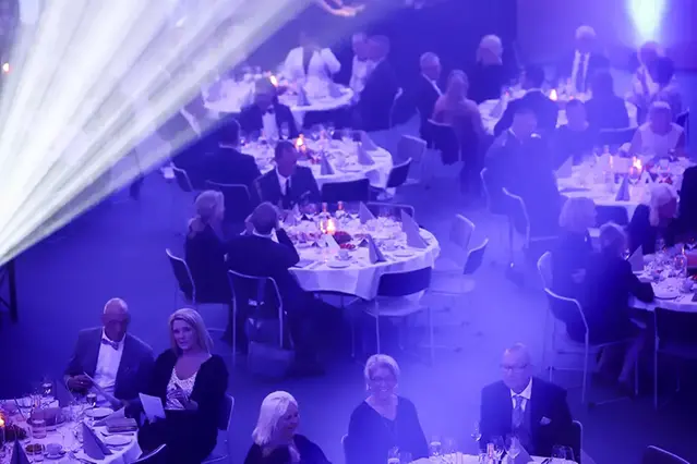 Många personer sitter runt festligt dukade bord. Dämpad belysning i blått.