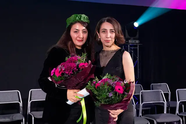 Två personer med blombuketter i händerna står på en scen.
