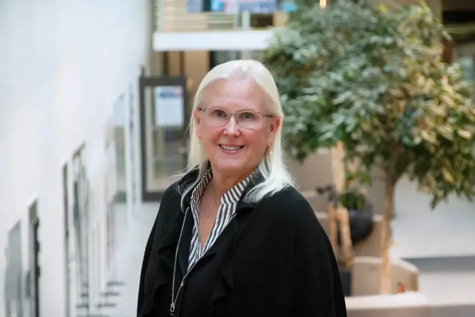 En person med långt ljust hår och glasögon ler in i kameran. Foto