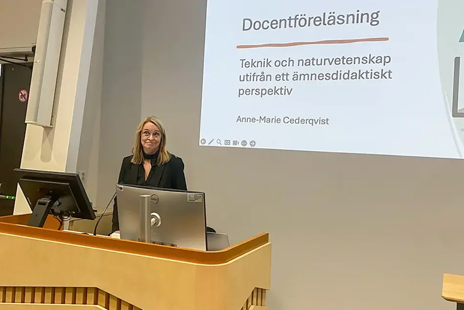 Person står bakom ett podium. I bakgrunden visas en presentationsbild med texten Docentföreläsning Teknik och naturvetenskap utifrån ett ämnesdidaktiskt perspektiv.. Foto