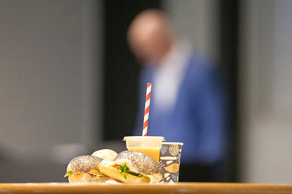 bread, juice and coffe. person in blue in the background. Photo.
