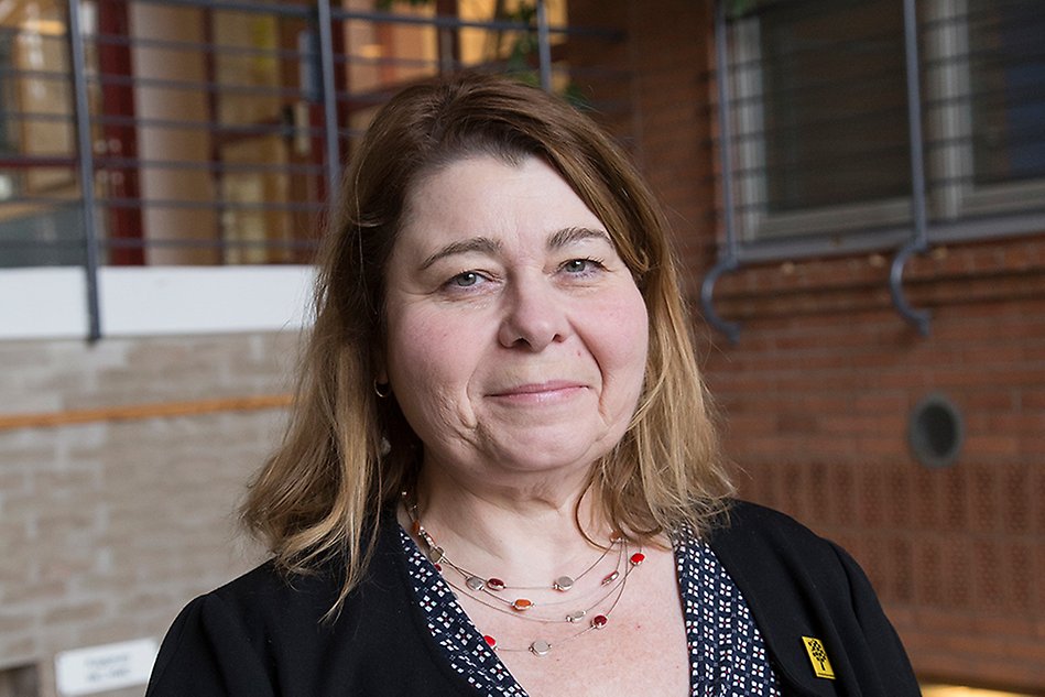Smiling woman with dark blonde hair, brick walls in the background. Photo.