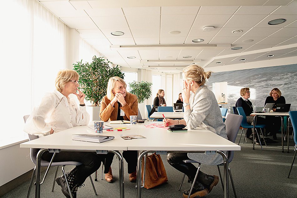 Tre personer sitter vi ett bord och pratar med varandra. Foto.