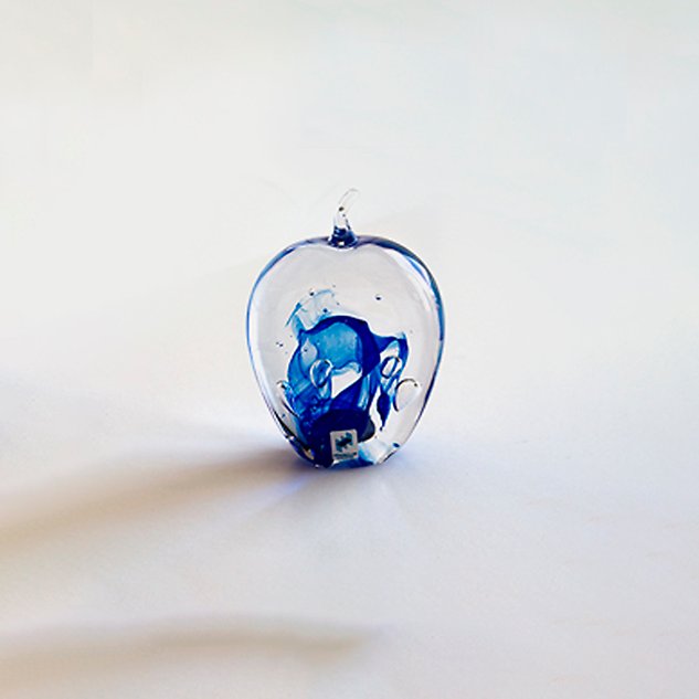 Glaskonst i form av ett äpple med blått mönster inuti. Foto.