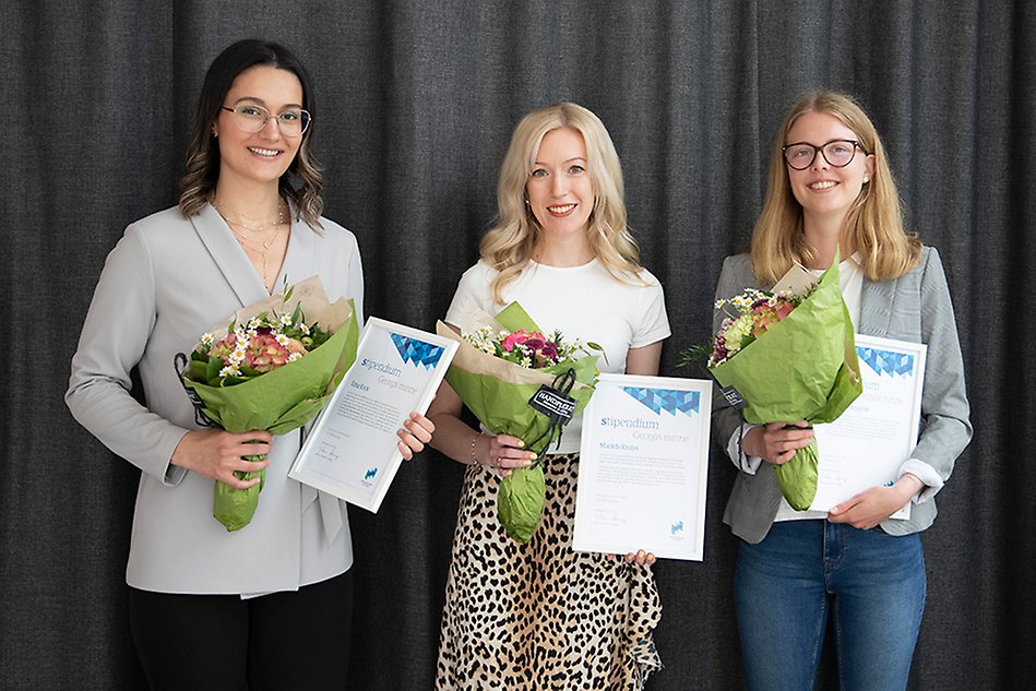 Tre unga kvinnor med diplom och blomsterbuketter i händerna,, grå bakgrund