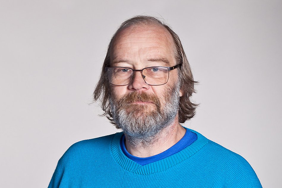 Portrait of a man with glasses and a beard, wearing a blue jumper. Photo.
