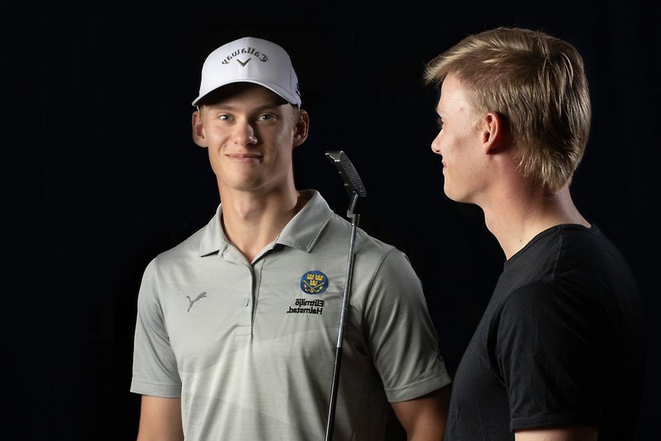 En blond student i svart t-shirt tittar på sin spegelbild. Spegelbilden är en avbild av han själv i golfkläder. Svart bakgrund. Foto.