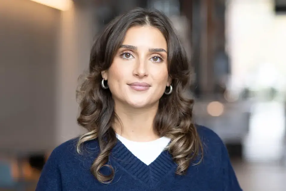 Porträtt på en kvinna som ler. I den suddiga, ljusa bakgrunden syns en korridor på campus. Foto.