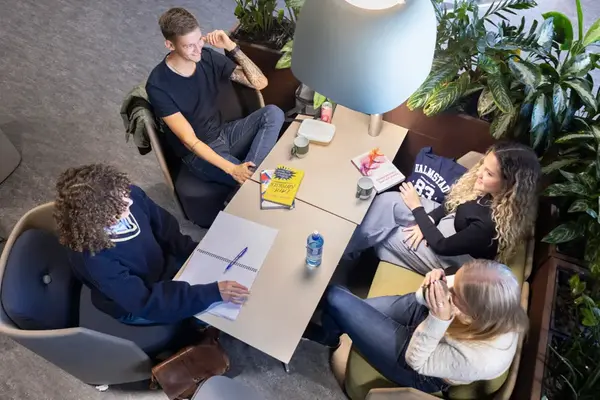 Fyra personer med anteckningsblock och pennor sitter runt ett bord. Bilden är tagen uppifrån.