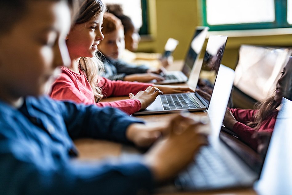 Close up photo from the side of four children looking at and typing on laptops. Photo