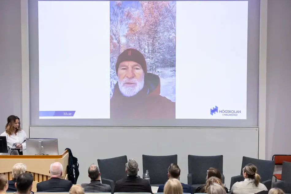 Person på en stor bildskärm framför publik. Foto