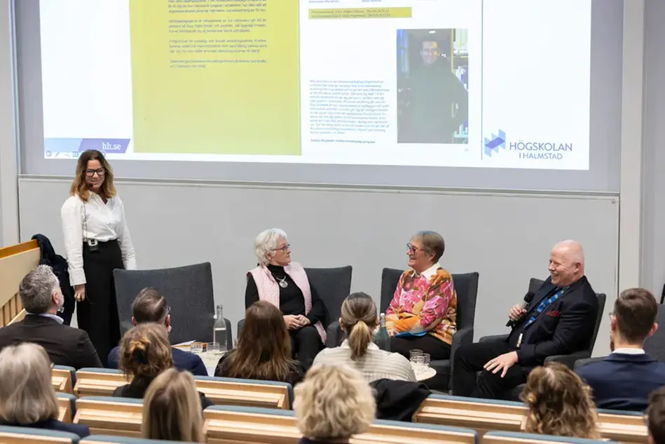 Tre personer sitter och samtalar framför en publik. Foto