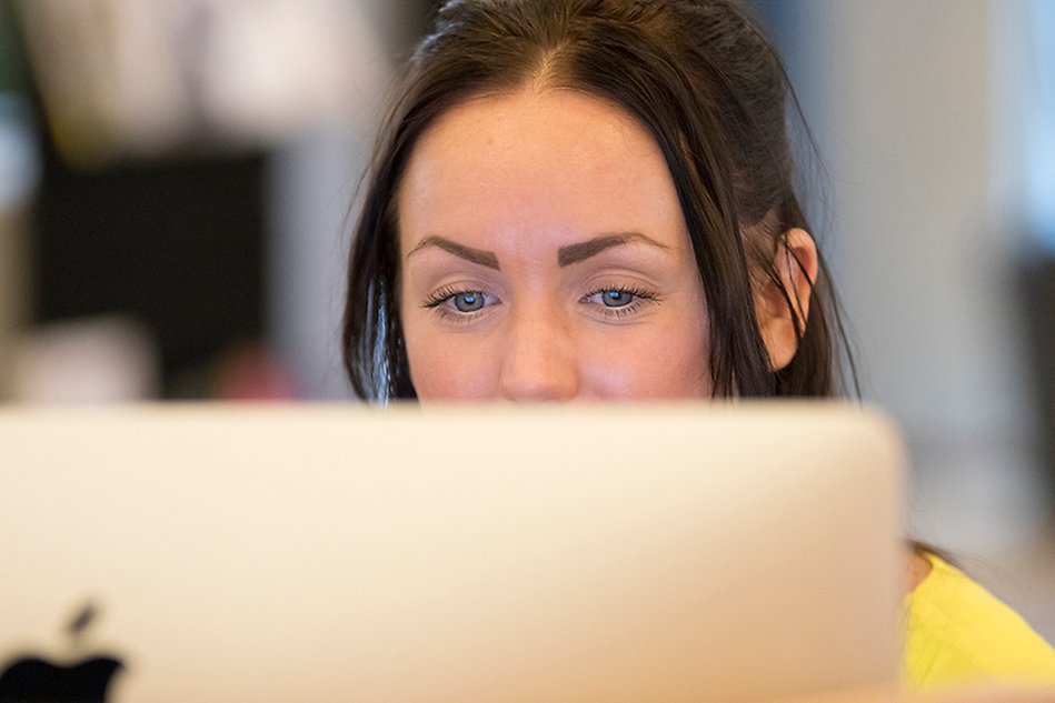 A woman looks at her computer screen. Parts of the face is covered by the screen. Photo. 