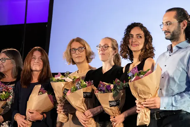 En grupp personer står och sitter på en scen och håller blommor i sina händer.