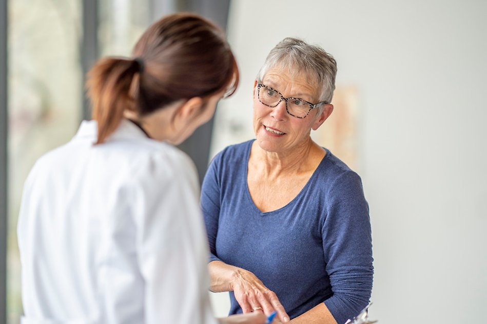 Woman in white, could be a medical doctor, talks to a woman in blue. Photo.