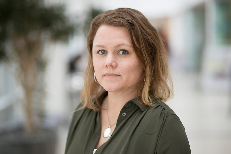 Portrait of a person looking into the camera. In the background one can see a corridor with green plants.  Photo. 