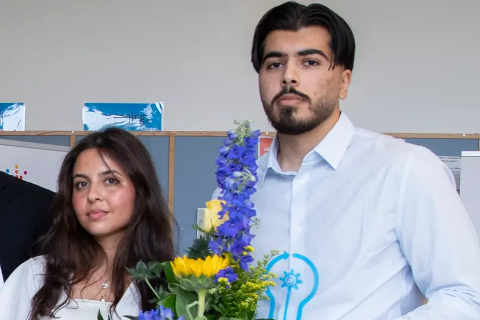 Två studenter med blommor och statyett ler mot kameran.. Foto.