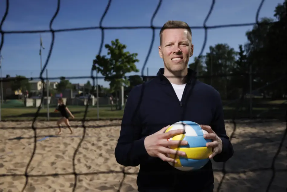 En man står på en beachvolleybollplan och håller i en boll. Foto.