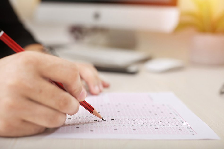 A pencil on a test sheet. Part of the hand holding the pencil is visible. Photo. 