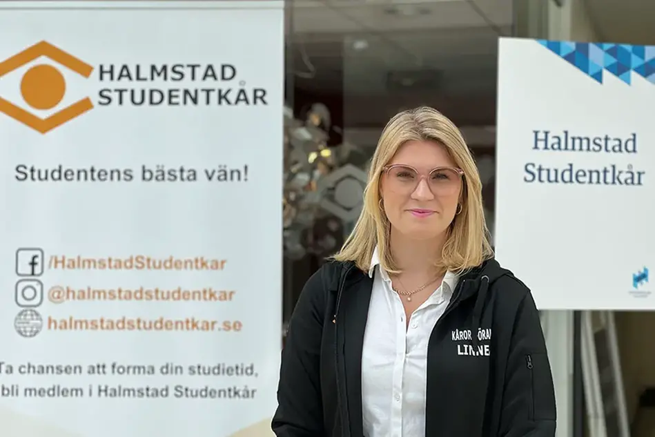 En kvinna mellan två informationsskyltar tittar in i kameran.