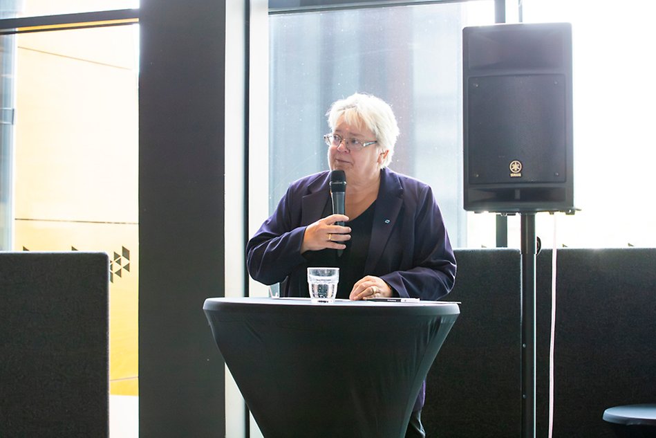 A woman stands at a podium with a microphone in her hand. Photo