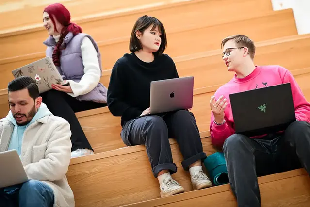 Four students sitting on the stairs at campus, studying with their laptops. Photo.
