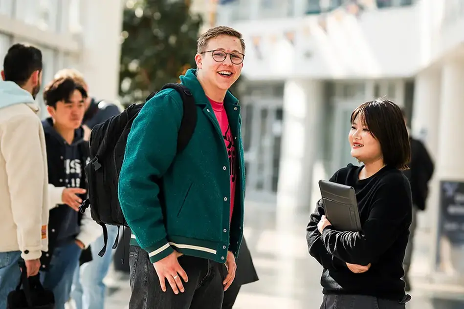 A young man and young woman talking in a hall at campus. Photo.