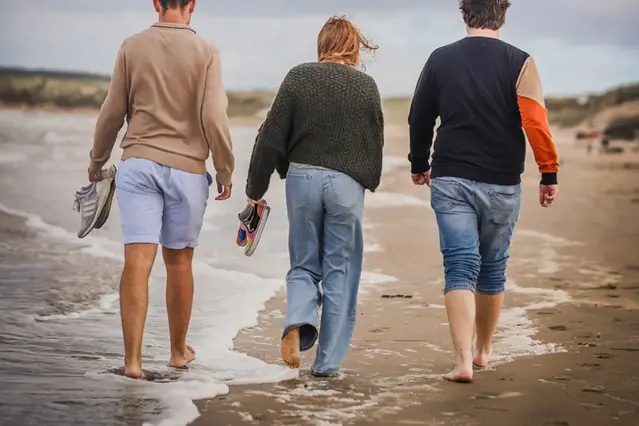 Three people strolling on the beach, seen rom behind. Photo.