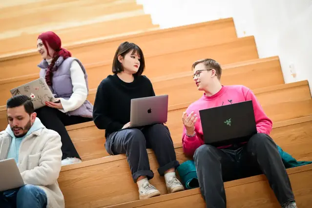 Fyra studenter sitter på en trappa och studerar med sina bärbara datorer. Foto.